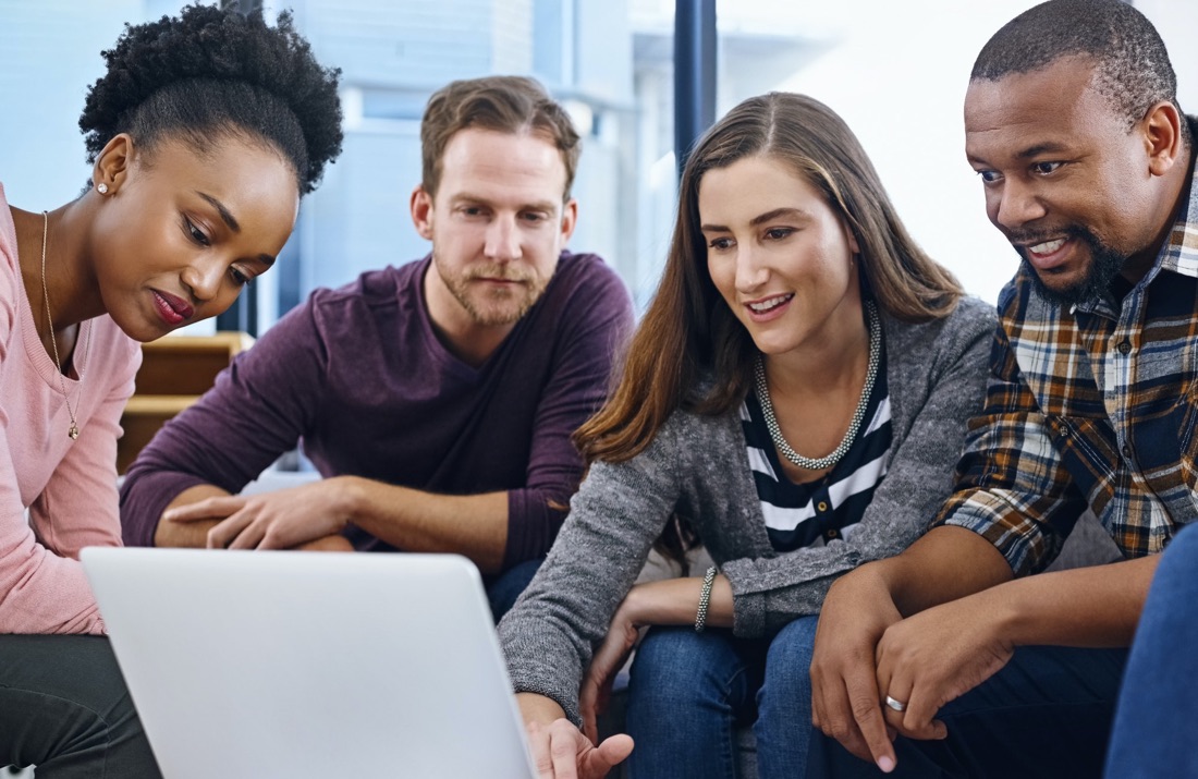 Four colleagues gathered around a laptop, reviewing work together.